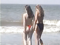 Two young blonde chicks walking on the sandy beach topless