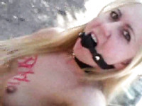 Wacky blonde whore with BDSM fetish stands naked outdoor wearing a mouth gag