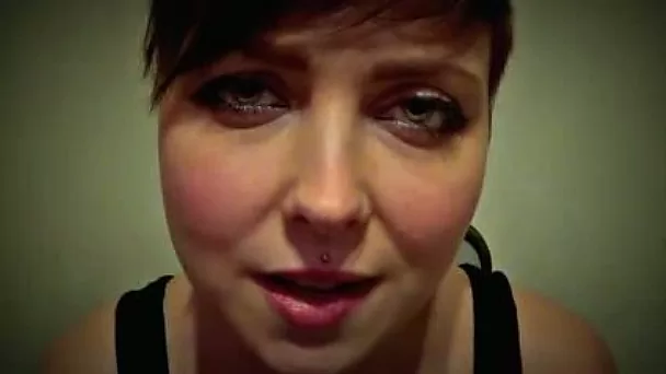 Short haired big eyed domme in black tank top whispers something erotic on webcam